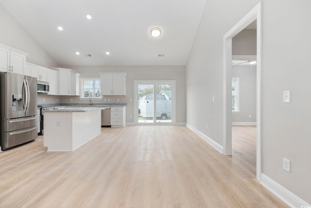 kitchen featuring appliances with stainless steel finishes, white cabinetry, lofted ceiling, a center island, and light stone countertops