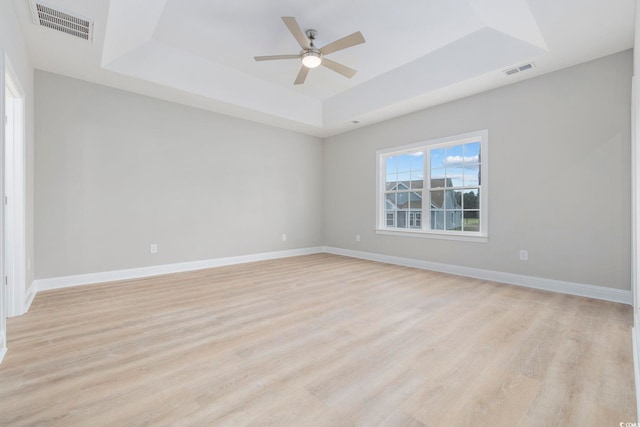 empty room with light hardwood / wood-style flooring, ceiling fan, and a tray ceiling