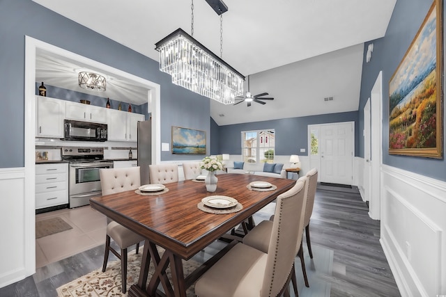 dining space featuring dark wood-type flooring, ceiling fan with notable chandelier, and vaulted ceiling