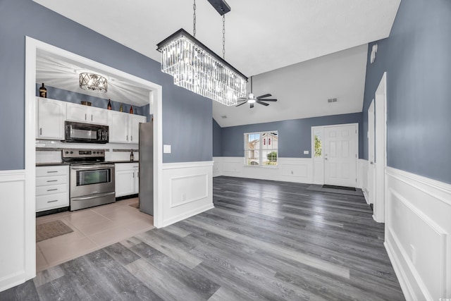 kitchen featuring decorative light fixtures, vaulted ceiling, hardwood / wood-style flooring, stainless steel appliances, and white cabinets