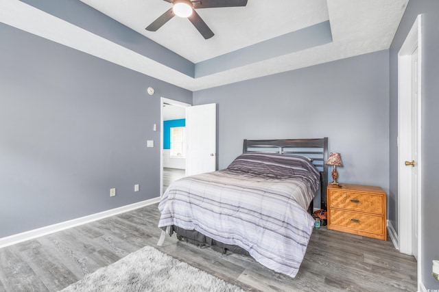 bedroom with a raised ceiling, ceiling fan, and dark hardwood / wood-style flooring