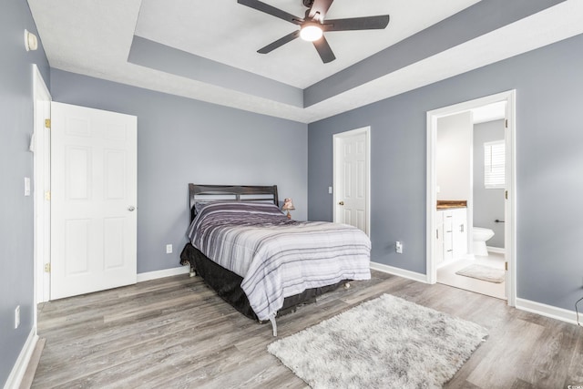 bedroom with hardwood / wood-style floors, a tray ceiling, ceiling fan, and ensuite bathroom