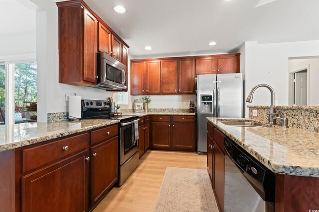 kitchen with stainless steel appliances, light stone countertops, sink, and light wood-type flooring