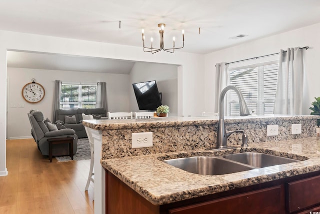 kitchen with sink, light stone counters, vaulted ceiling, light wood-type flooring, and a notable chandelier