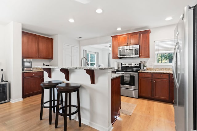 kitchen featuring light hardwood / wood-style flooring, a kitchen island with sink, stainless steel appliances, light stone counters, and a kitchen bar