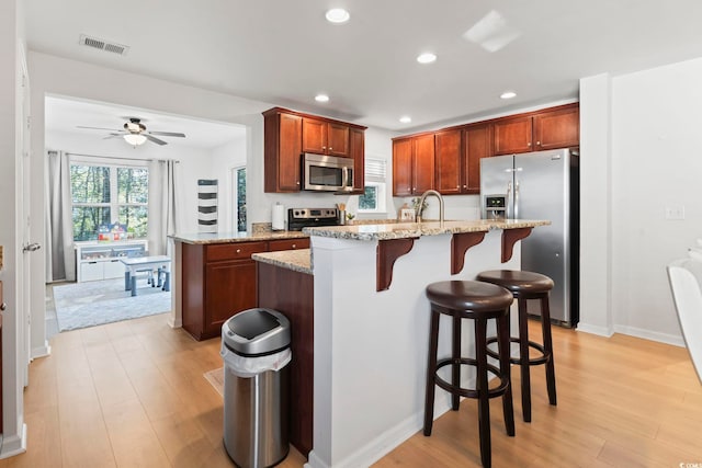 kitchen with sink, appliances with stainless steel finishes, a kitchen breakfast bar, light stone countertops, and light hardwood / wood-style floors