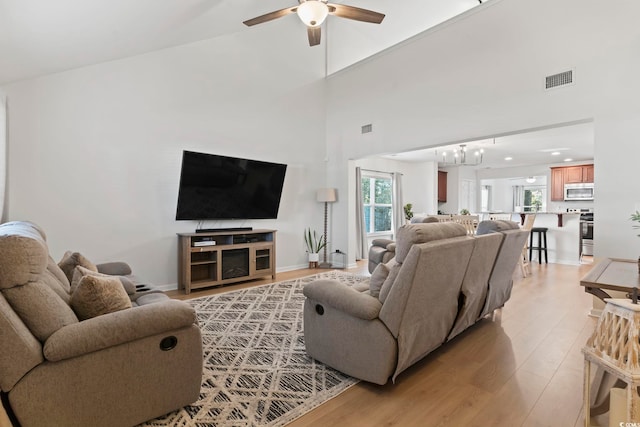 living room with a high ceiling, ceiling fan, and light hardwood / wood-style floors