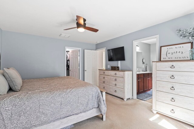 bedroom with connected bathroom, a walk in closet, light colored carpet, ceiling fan, and a closet