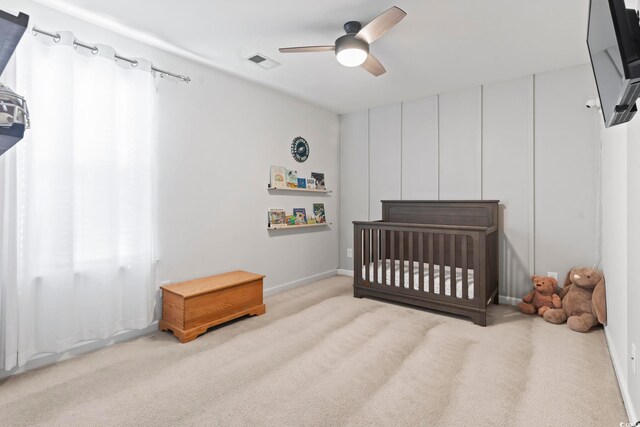 carpeted bedroom featuring a crib and ceiling fan