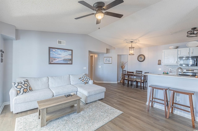 living room featuring lofted ceiling, a textured ceiling, visible vents, a ceiling fan, and light wood-type flooring