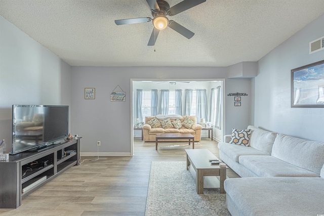 living area with visible vents, light wood-style flooring, ceiling fan, a textured ceiling, and baseboards