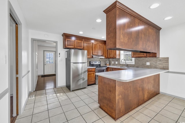 kitchen with sink, light tile patterned floors, kitchen peninsula, stainless steel appliances, and backsplash