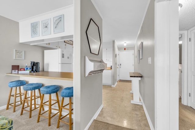 kitchen with a breakfast bar, white cabinetry, crown molding, white refrigerator, and kitchen peninsula