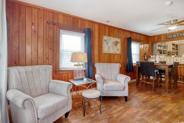 living area featuring wood-type flooring, ceiling fan, and wooden walls