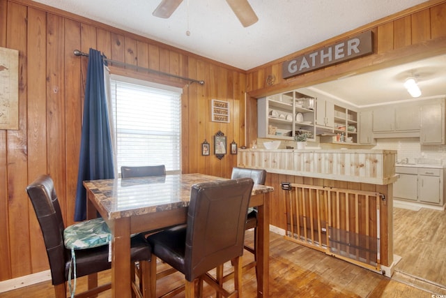 dining space with crown molding, ceiling fan, wooden walls, and light hardwood / wood-style flooring