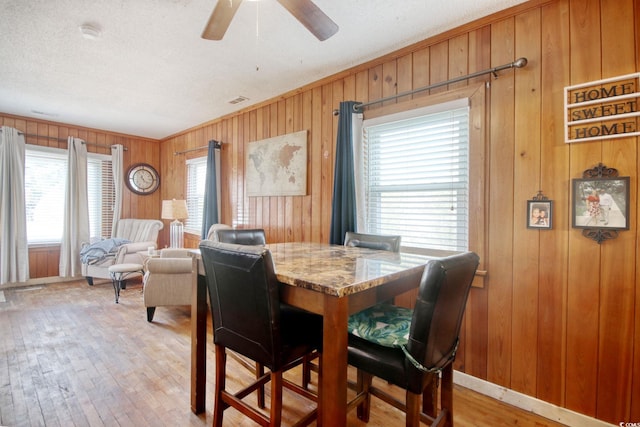 dining area with ornamental molding, wood walls, ceiling fan, and light wood-type flooring