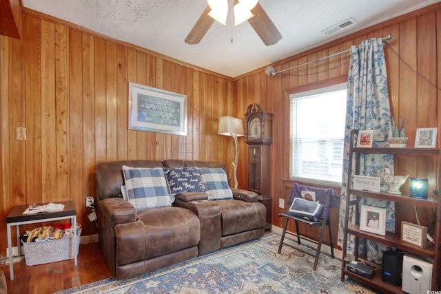 living room featuring hardwood / wood-style flooring, ceiling fan, and wood walls