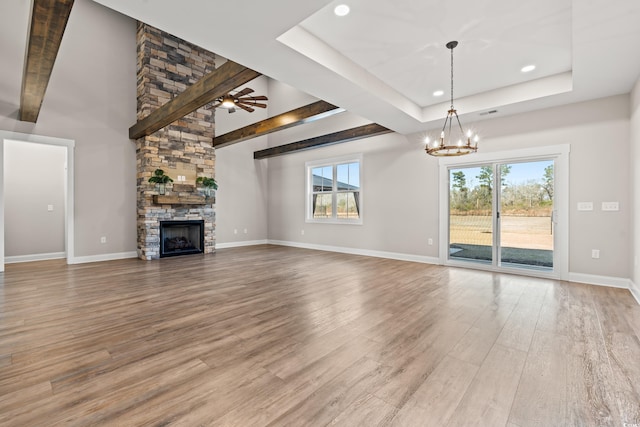 unfurnished living room featuring a tray ceiling, a healthy amount of sunlight, a stone fireplace, and wood finished floors