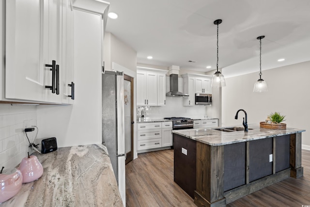 kitchen featuring a sink, white cabinets, hanging light fixtures, appliances with stainless steel finishes, and wall chimney exhaust hood