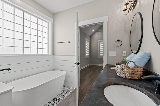 bathroom featuring wood finished floors, a sink, vaulted ceiling, a soaking tub, and double vanity