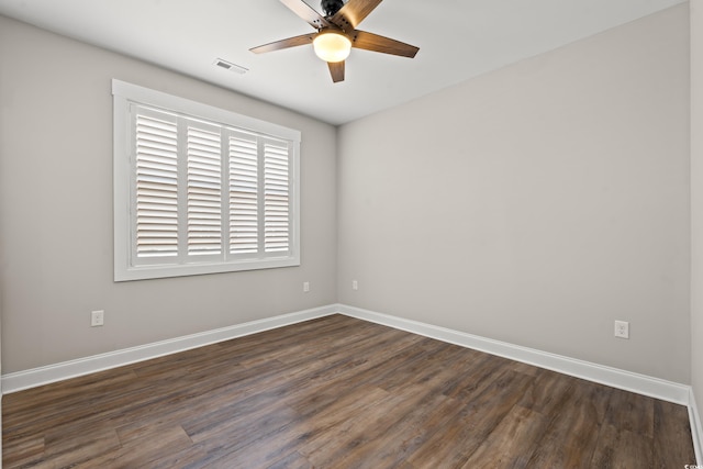 spare room with dark wood-style flooring, visible vents, and baseboards