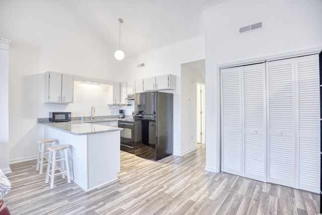 kitchen with pendant lighting, high vaulted ceiling, black appliances, kitchen peninsula, and light wood-type flooring