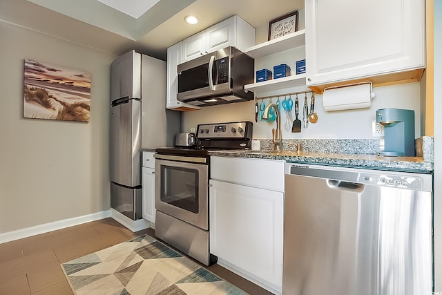 kitchen featuring dark stone countertops, stainless steel appliances, sink, and white cabinets