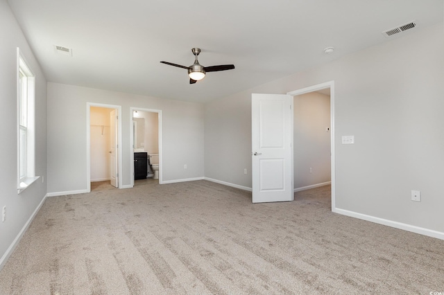 unfurnished bedroom with ceiling fan, a walk in closet, ensuite bathroom, and light carpet