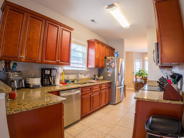 kitchen with sink, appliances with stainless steel finishes, light stone countertops, a healthy amount of sunlight, and light tile patterned flooring