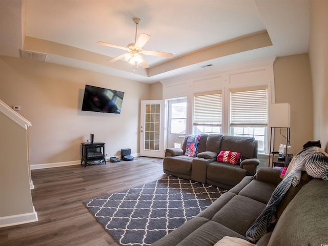 living room with dark hardwood / wood-style floors, a raised ceiling, ceiling fan, and a wood stove