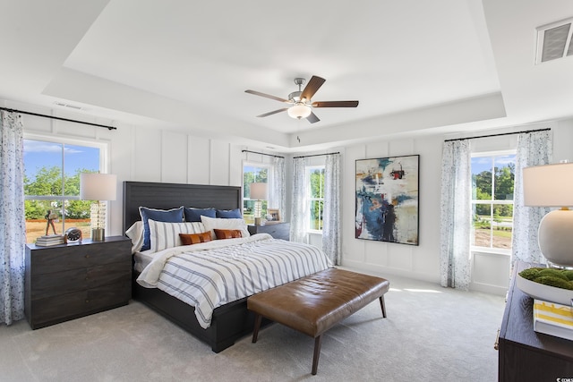 bedroom with multiple windows, a raised ceiling, light carpet, and ceiling fan