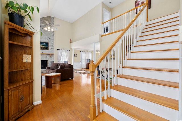 staircase with hardwood / wood-style flooring, a large fireplace, ceiling fan, and high vaulted ceiling