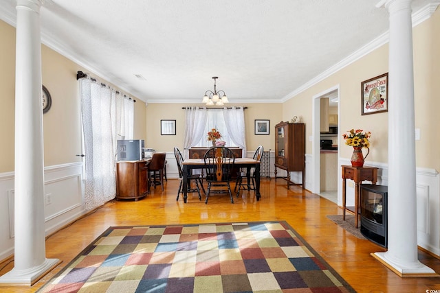 dining room featuring a notable chandelier, crown molding, decorative columns, and light wood-type flooring