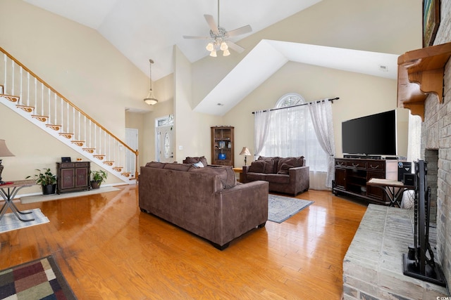 living room with a brick fireplace, light hardwood / wood-style flooring, high vaulted ceiling, and ceiling fan