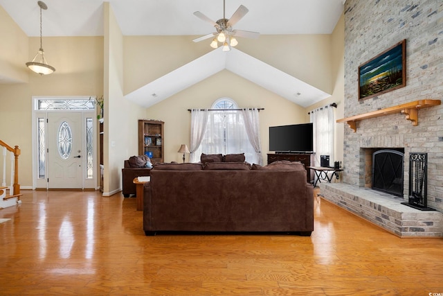 living room featuring ceiling fan, high vaulted ceiling, a fireplace, and light hardwood / wood-style flooring