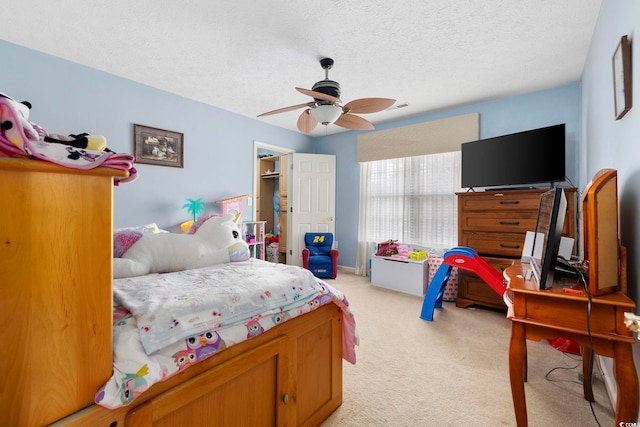 carpeted bedroom with ceiling fan, a spacious closet, and a textured ceiling