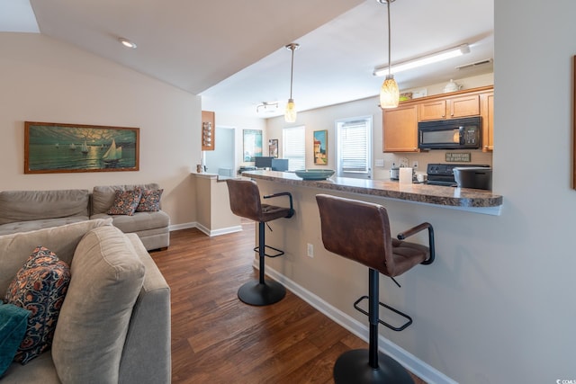 kitchen featuring black appliances, dark hardwood / wood-style flooring, a kitchen bar, hanging light fixtures, and kitchen peninsula