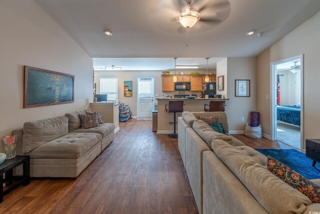 living room with dark wood-style flooring, a ceiling fan, and baseboards