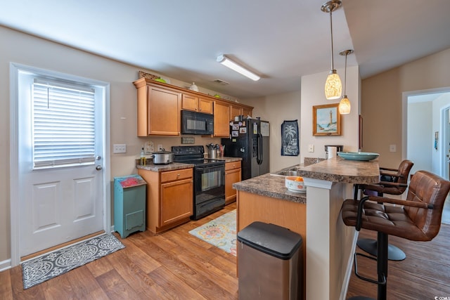 kitchen featuring a breakfast bar, pendant lighting, dark countertops, light wood-type flooring, and black appliances