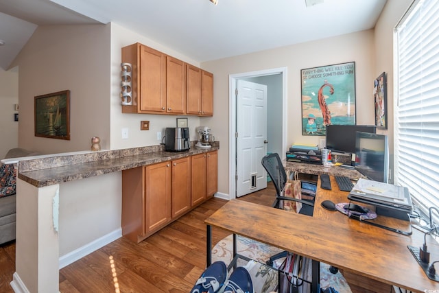 interior space with light wood finished floors, baseboards, brown cabinetry, dark countertops, and a peninsula