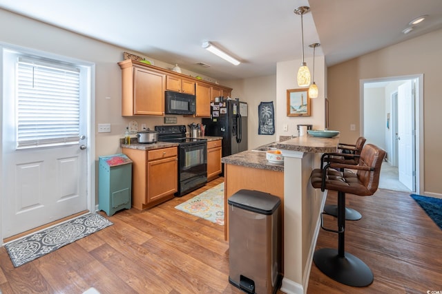 kitchen with light wood-type flooring, a breakfast bar area, dark countertops, and black appliances