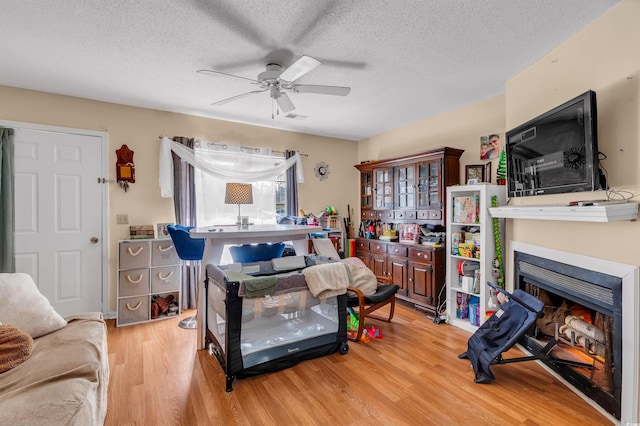 living room with ceiling fan, a textured ceiling, and light wood-type flooring