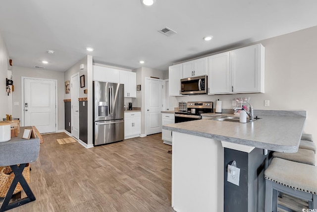 kitchen with sink, stainless steel appliances, a kitchen breakfast bar, white cabinets, and light wood-type flooring