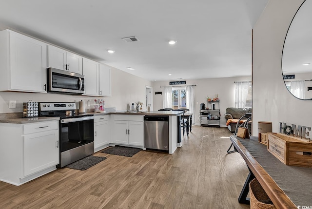 kitchen with sink, kitchen peninsula, stainless steel appliances, light hardwood / wood-style floors, and white cabinets