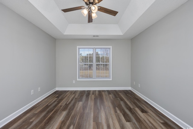 spare room featuring dark wood-type flooring, ceiling fan, and a tray ceiling