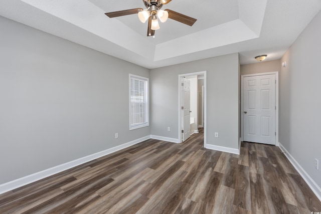 unfurnished bedroom featuring ceiling fan, connected bathroom, dark hardwood / wood-style flooring, and a tray ceiling