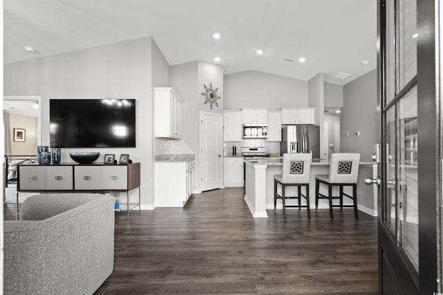 kitchen with dark wood-type flooring, appliances with stainless steel finishes, a kitchen breakfast bar, white cabinets, and decorative backsplash