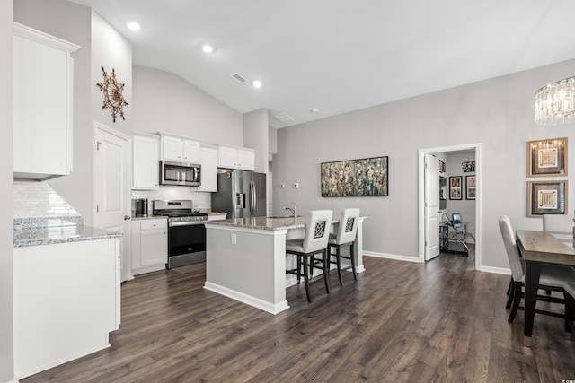 kitchen featuring dark hardwood / wood-style floors, white cabinetry, an island with sink, stainless steel appliances, and light stone countertops