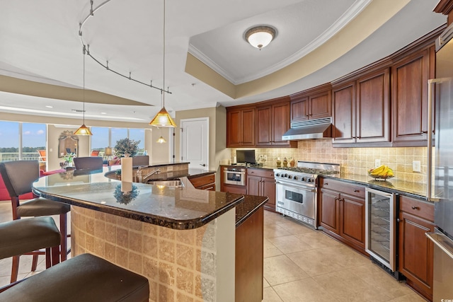 kitchen featuring high quality appliances, hanging light fixtures, a raised ceiling, beverage cooler, and a kitchen bar