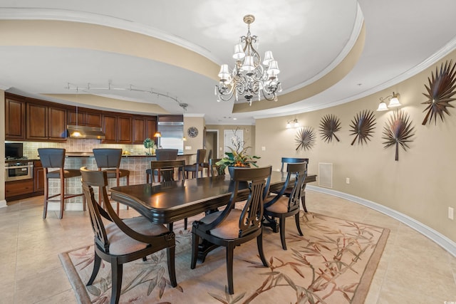 dining space with light tile patterned floors, a chandelier, a raised ceiling, track lighting, and ornamental molding